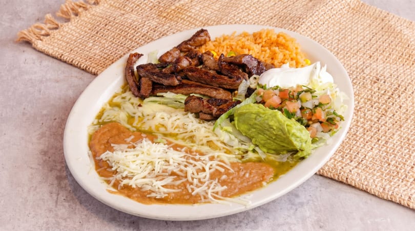 A white oval plate holds steak, rice, beans, guacamole, pico de gallo, and sour cream.